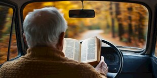 老人驾车途中专注看书