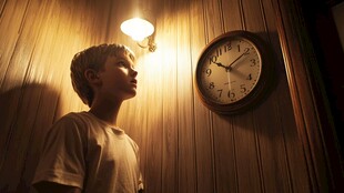 男孩在灯光下凝视墙上时钟