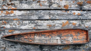 老旧木舟靠于斑驳木墙前